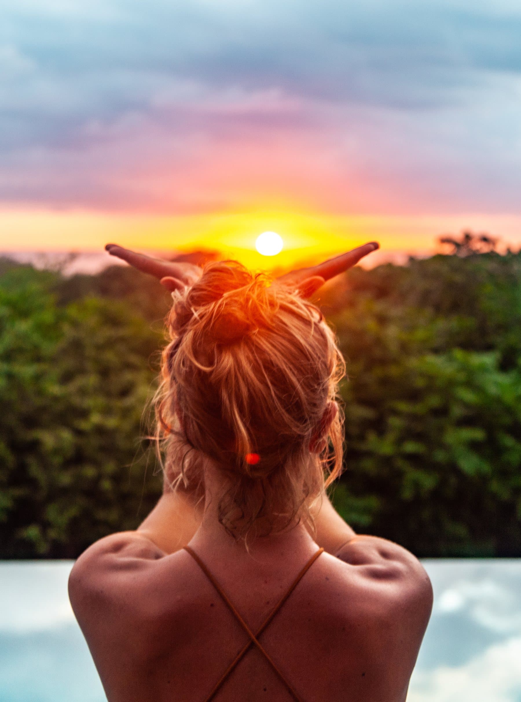 Frau mit roten Haaren streckt bei Sonnenuntergang über dem Dschungel die Arme dem Himmel entgegen